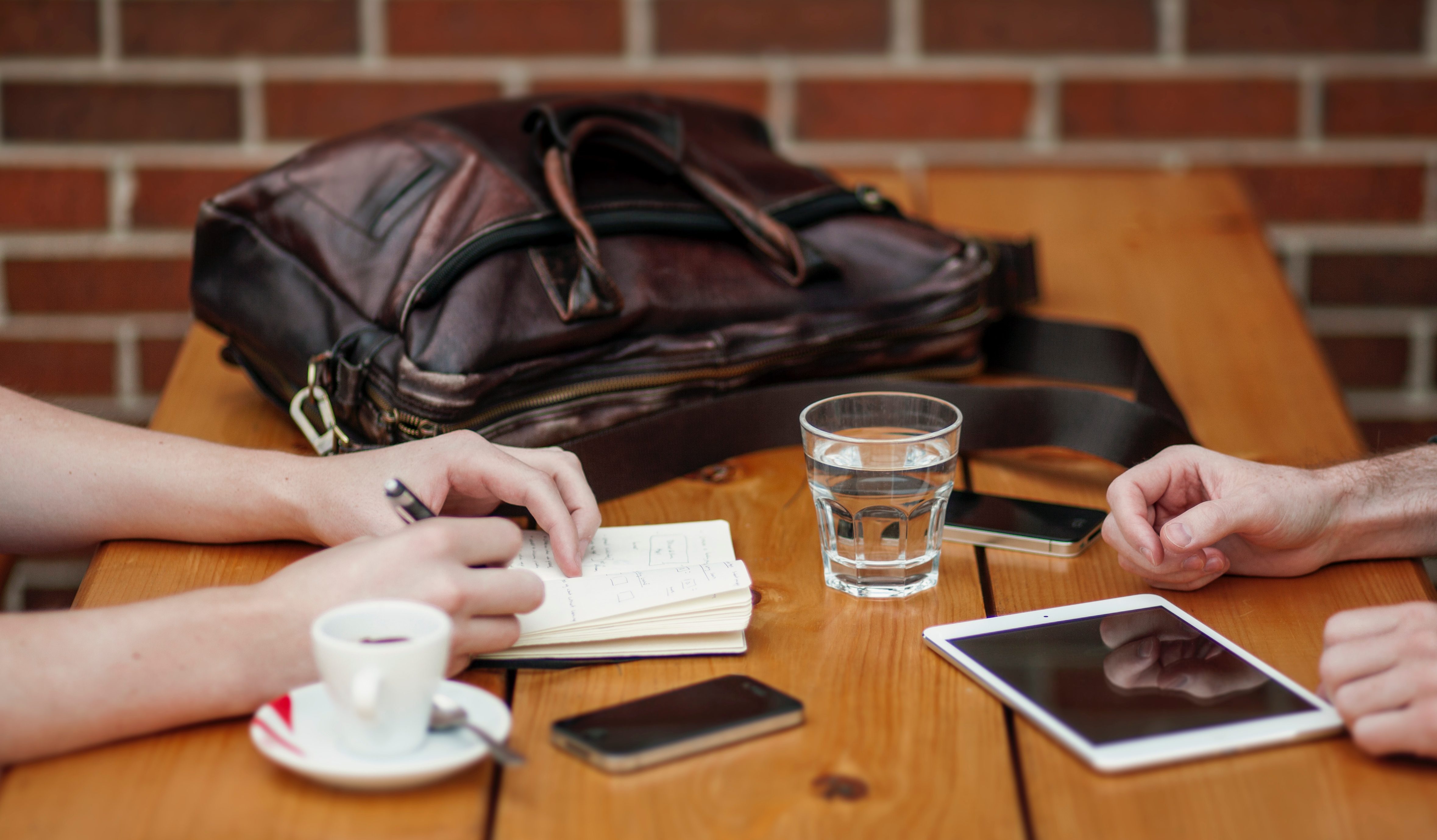 Close up of hands on a table surrounded by cups and electronic equipment and note books